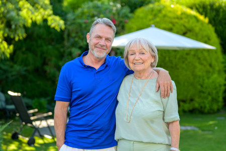 A mature man and an elderly woman standing close together, smiling warmly and enjoying a sunny day in a lush green garden.の写真素材