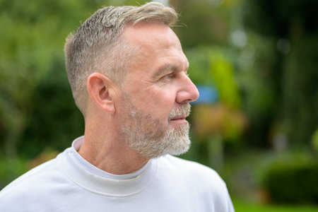 A close-up side profile of a mature man with a neatly trimmed gray beard and short hair, dressed in a white shirt.の写真素材