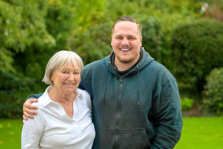 A warm and joyful portrait featuring a young man and an older woman standing together in a lush green garden.の写真素材
