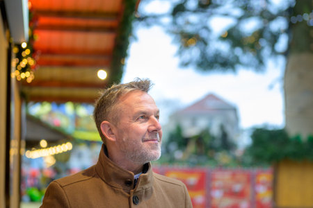 A man in a beige coat gazes upward with a peaceful expression, standing amidst the cozy ambiance of...