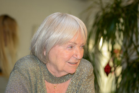 An elderly woman with silver hair and a warm smile is dressed in a shimmering silver outfit with a...