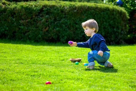 A toddler crouches with focus and energy, holding a purple Easter egg while reaching for more.