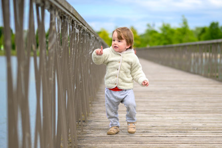 Little toddler in a fluffy jacket and sweatpants walking across a wooden bridge.