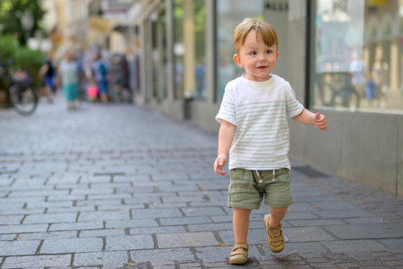 Adorable young boy walking confidently along a cobblestone pedestrian street in a city center.