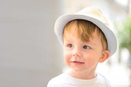 Close-up of a smiling toddler boy wearing a light summer hat and a white t-shirt.