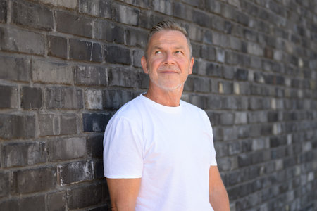 Color portrait of a confident senior man standing in front of a brick wall.の写真素材