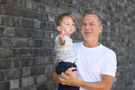 An elderly man in a white shirt holds a young boy who is pointing at something in the distance.の写真素材