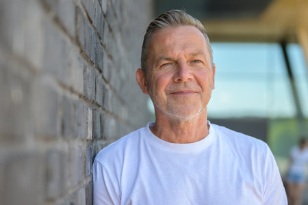 Portrait of a mature man with a short haircut and slight smile, standing in front of a gray brick wall.の写真素材