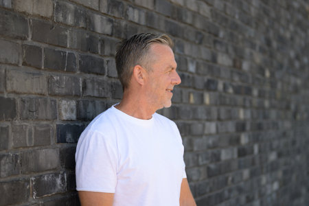 Side profile portrait of a mature man standing against a textured gray brick wall.の写真素材