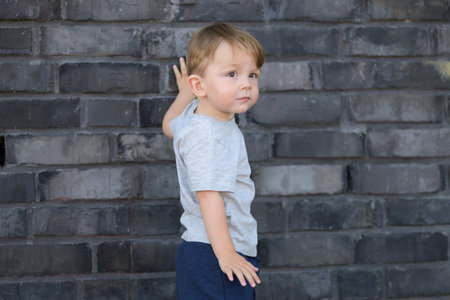 Side profile of a young boy standing in front of a textured brick wall, gently touching it with one hand while looking attentively into the distance.の写真素材