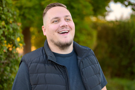 A joyful young man laughs openly while standing outdoors in a natural green environment during daylight.の写真素材