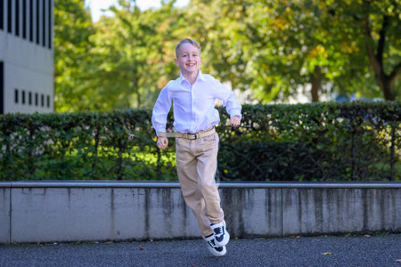 Cheerful young boy wearing a white shirt and beige pants running joyfully outside on a sunny day with trees in the background.の写真素材