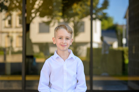 Portrait of a young boy with blond hair wearing a white shirt, smiling confidently in bright daylight with soft background blur.の写真素材