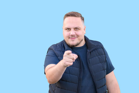 A confident young man with a friendly smile points directly at the camera against a light blue background.の写真素材