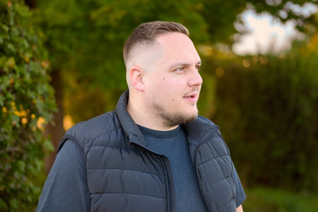 A young man with a calm and focused expression looks thoughtfully into the distance while standing outdoors in a green natural environment.の写真素材