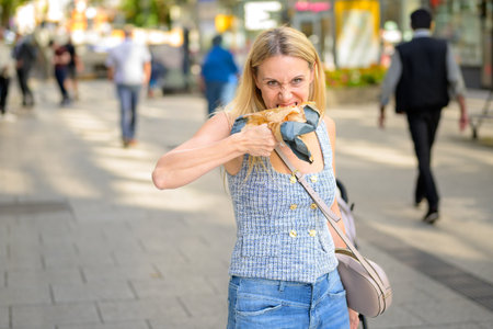 Blonde woman on a city street eating a slice of pizza wrapped in paper.の写真素材