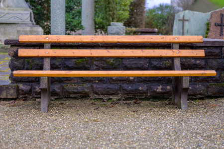 Empty wooden bench in a cemetery with gravestones in background, symbolizing mourning, remembrance,...