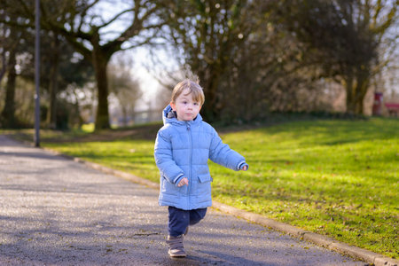 Young toddler walking confidently alone on sunny park path. Authentic childhood lifestyle scene...