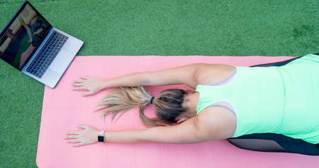 A woman doing an online yoga class in the garden of her house. We can see a close-up of her right...