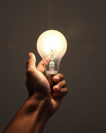 Hand holding a lightbulb on a dark background, energy concept