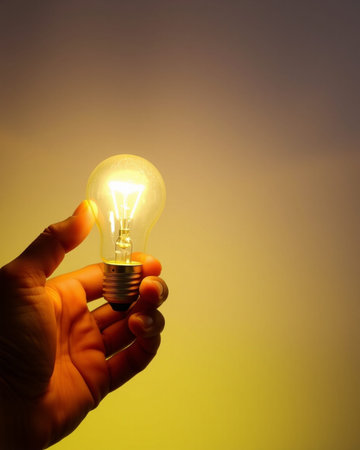 Hand holding a light bulb on yellow background with copy space for text