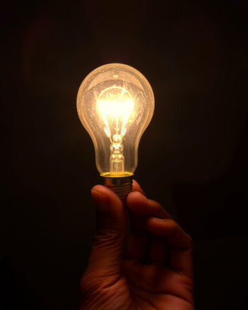 Hand holding a lightbulb on a black background with copy space
