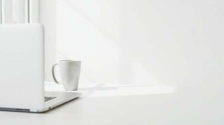 Laptop and coffee cup on white background with shadow from the window.