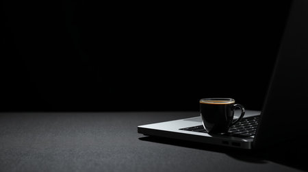 Coffee cup and laptop on black background, business concept.