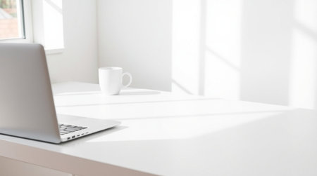 Laptop and coffee cup on white table in front of window.