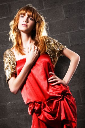 Fashionable red-haired woman in a satin red dress against brick wall background の写真素材
