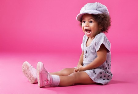 Portrait of a little girl in stylish clothing sitting on pink background and playing up の写真素材
