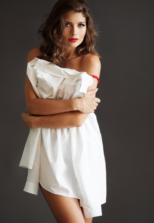 Beautiful lady hiding behind white shirt against dark gray backgroundの写真素材