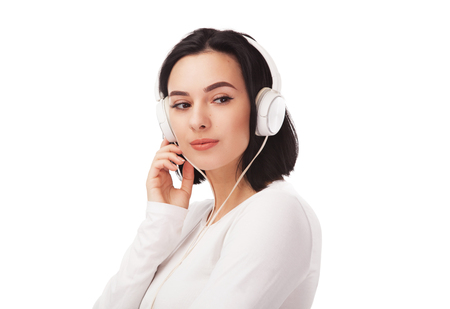 Young beautiful woman listening the music with curiosity in big headphones against white backgroundの写真素材