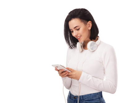 Young beautiful woman with smartphone and headphones against white backgroundの写真素材