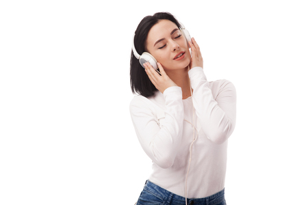 Young beautiful woman enjoying with listening the music in headphones against white backgroundの写真素材