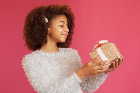 Cute festive girl holding a shiny gift box against pink backgroundの写真素材