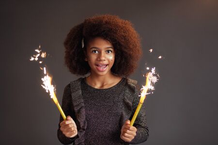 Cute festive girl with burning sparklers against dark backgroundの写真素材