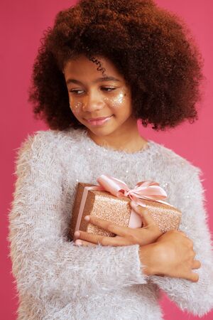 Cute festive girl holding a shiny gift box against pink backgroundの写真素材