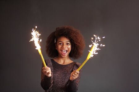 Cute festive girl with burning sparklers against dark backgroundの写真素材