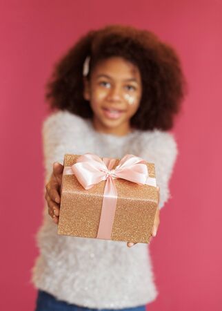 Cute festive girl giving a gift box against pink backgroundの写真素材