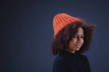 Lovely stylish teenage girl wearing bright knit hat against dark backgroundの写真素材