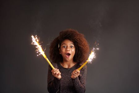 Cute festive girl with burning sparklers against dark backgroundの写真素材