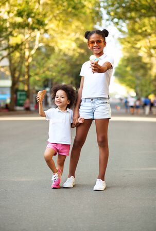 Summer days. Two little sisters with ice-cream in the streetの写真素材