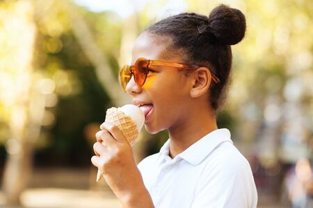 Cute girl in bright sunglasses eating ice-cream in the streetの写真素材