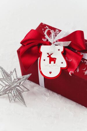 Christmas gift box with a bow wrapped in red surrounded by artificial snow and decorationの写真素材