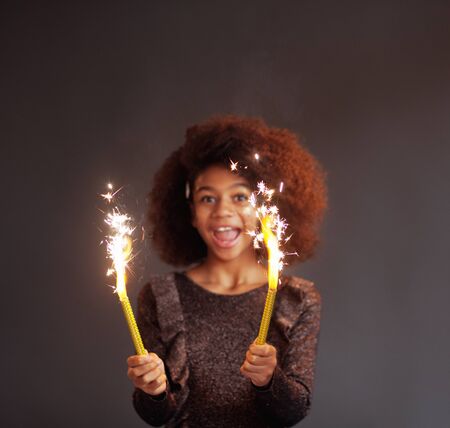 Cute festive girl with burning sparklers against dark background. Focus on sparklersの写真素材
