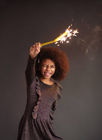 Cute festive girl with burning sparkler against dark backgroundの写真素材