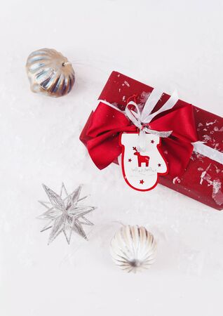 Christmas gift box with a bow wrapped in red surrounded by artificial snow and decorationの写真素材