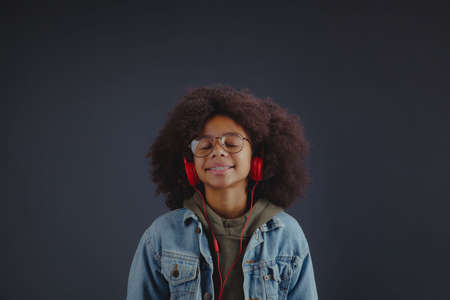 Cute tenage girl enjoying the music in headphones against dark background