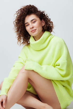 Portrait of beautiful woman with curly hair in warm cozy sweater against light backgroundの写真素材